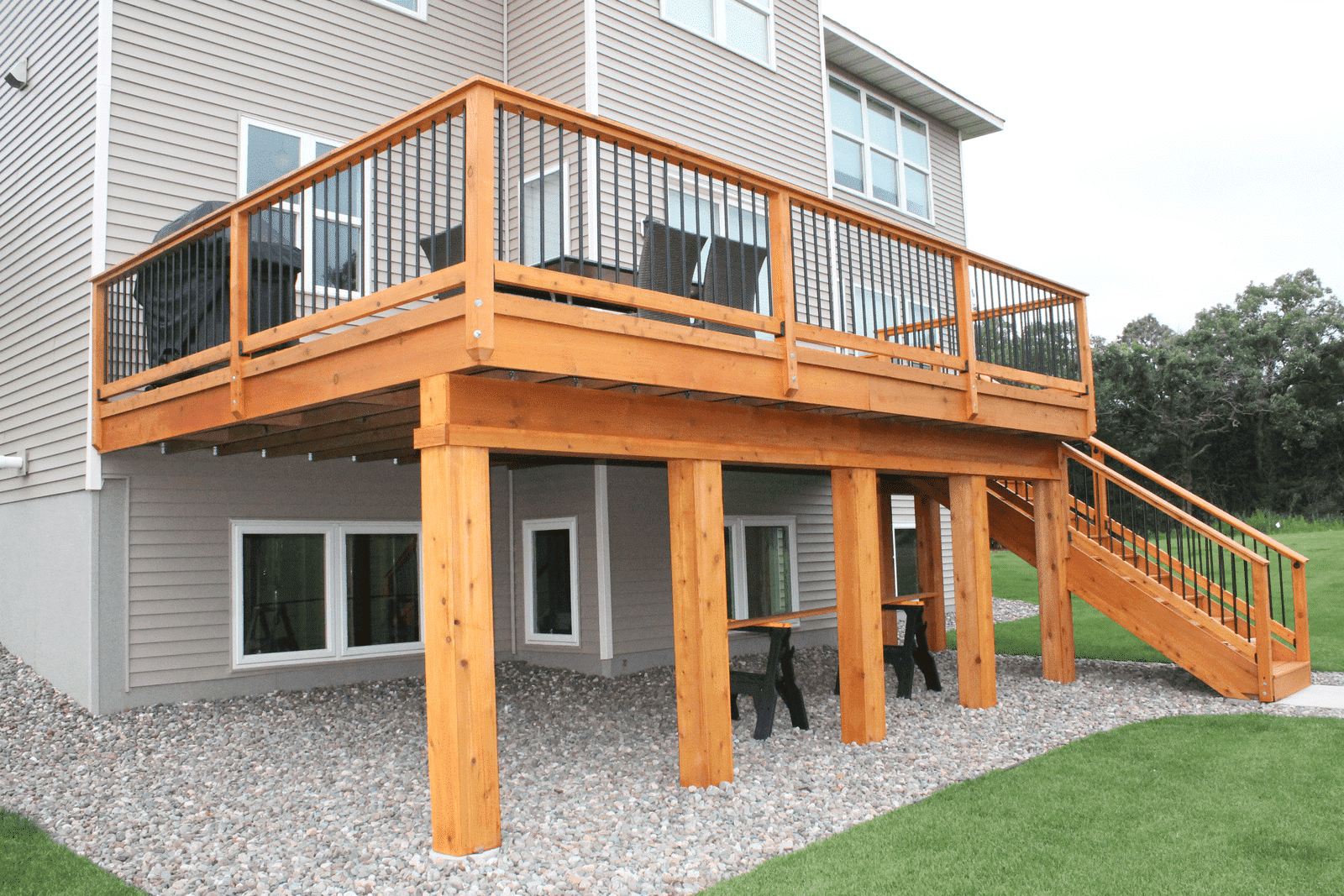 Elevated wooden deck with black metal railings, stairs, and a lower gravel patio